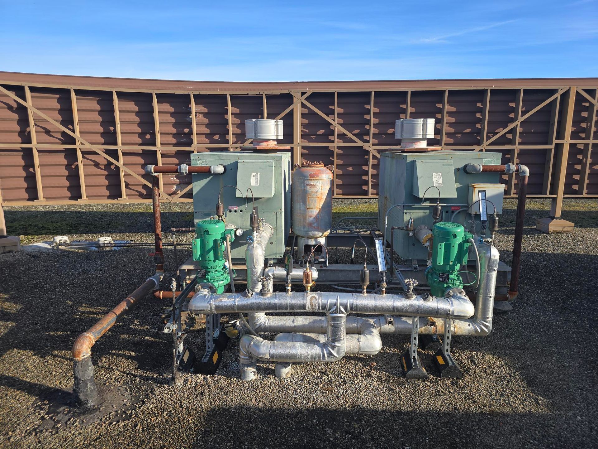 Two green industrial pumps on gravel in front of a freight railcar