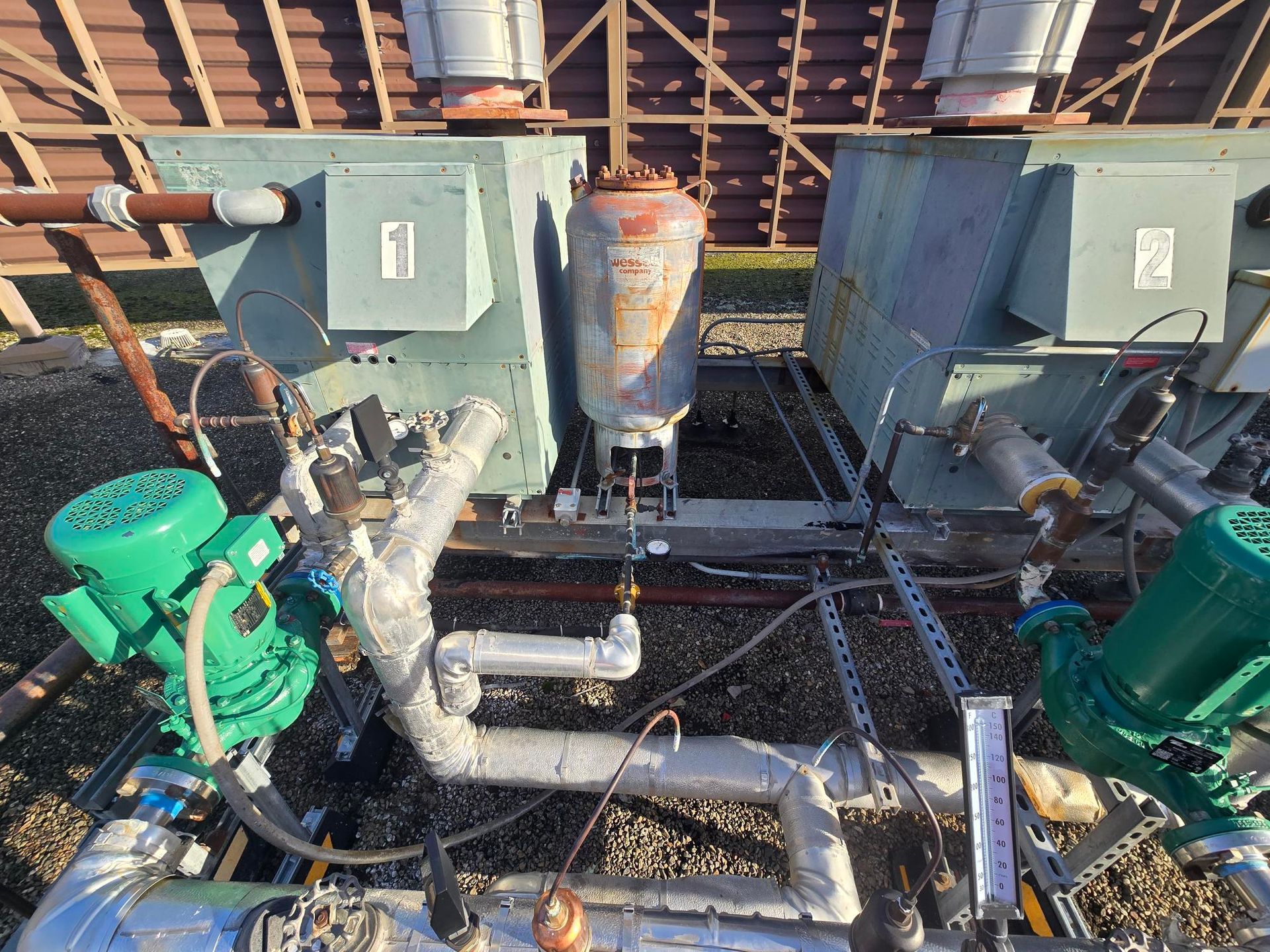 Industrial pumps and piping with green motors in a mechanical room under a wooden roof