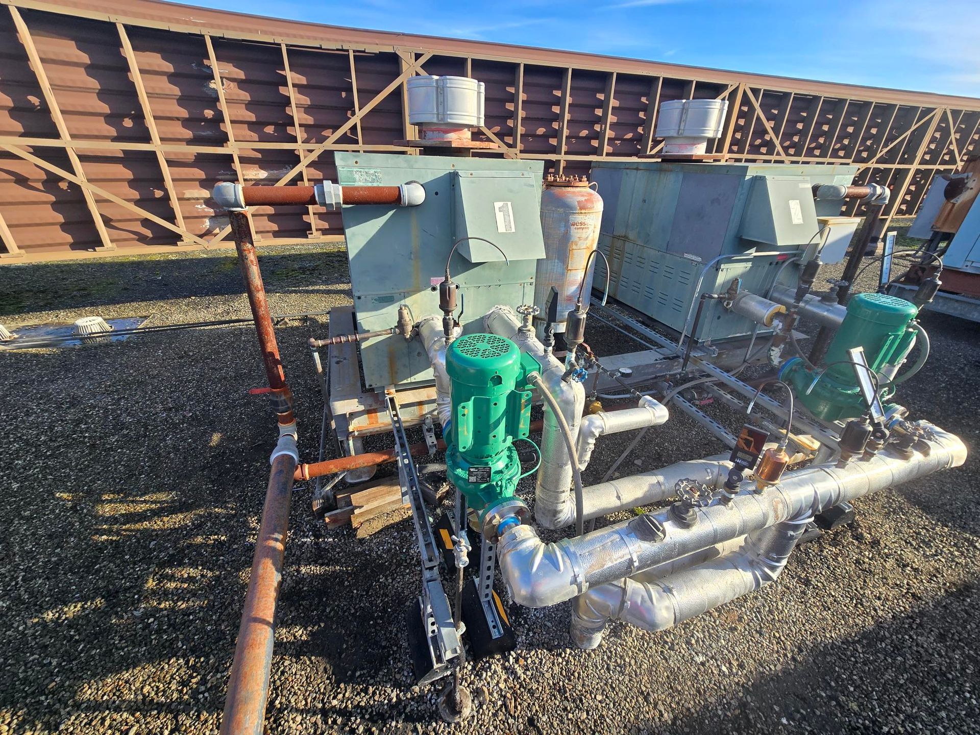 Industrial pumps and piping beside a large tank, with a worker standing nearby outdoors.
