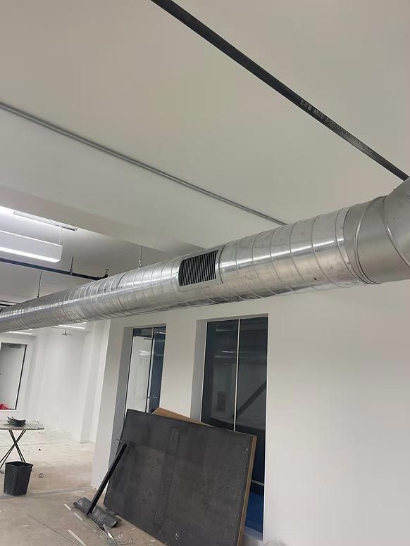 Office interior with exposed silver HVAC ducting and stacked panels along a white wall