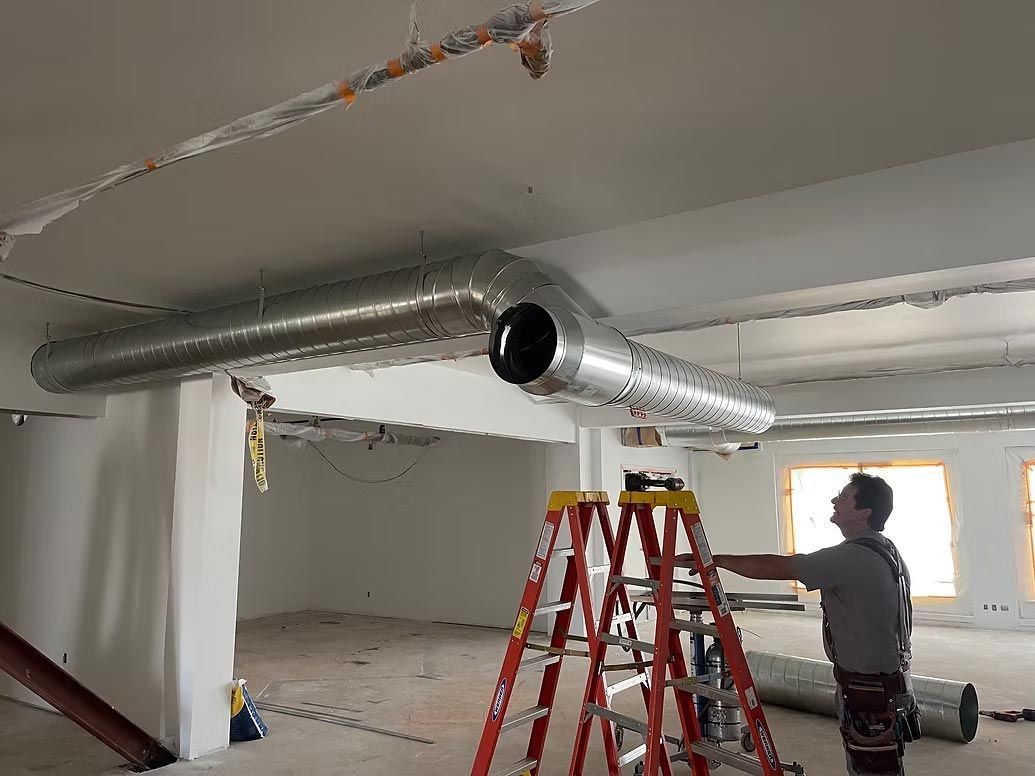 Worker inspecting ducting in a room under construction with ladders and exposed ceiling pipes