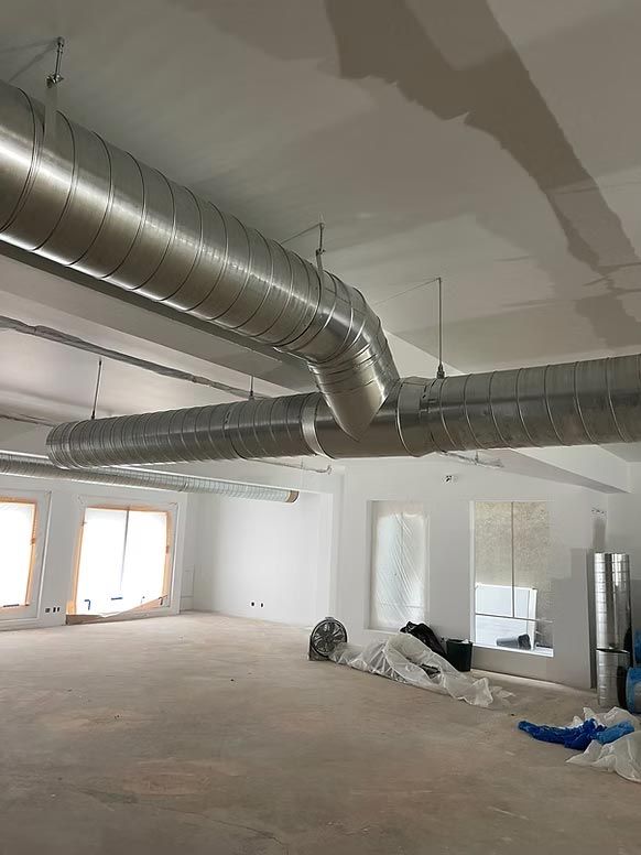 Interior of unfinished room with exposed ductwork, white walls, windows, and construction materials on the floor
