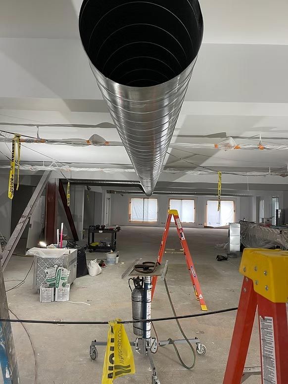 Indoor construction site with HVAC ductwork, red ladder, and tools in an unfinished room