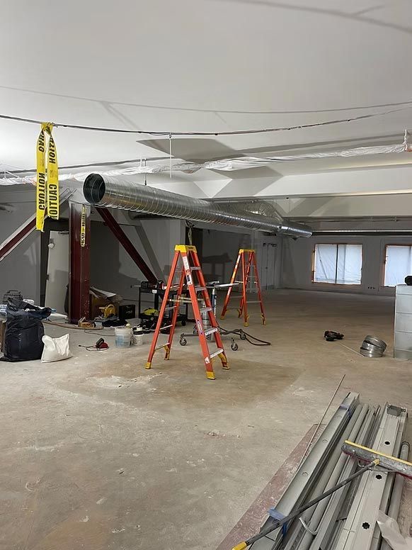 Partially renovated basement with ladders, tools, and construction materials on a concrete floor