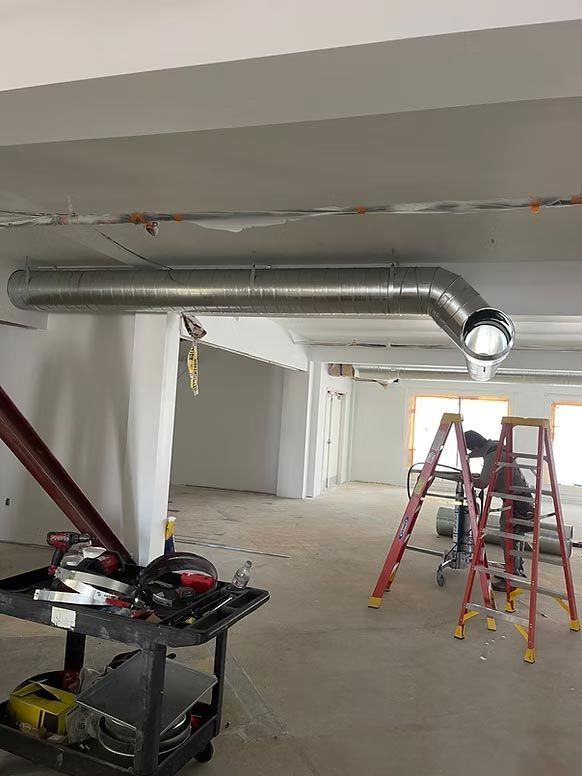 Renovation scene with exposed ductwork, ladders, and tools in a partially finished room