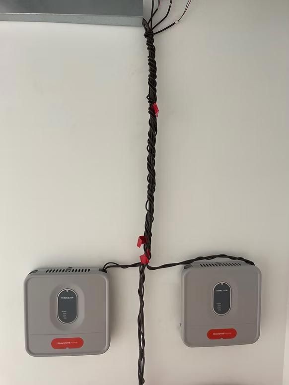 Two gray wall-mounted units connected by a black cable on a white wall