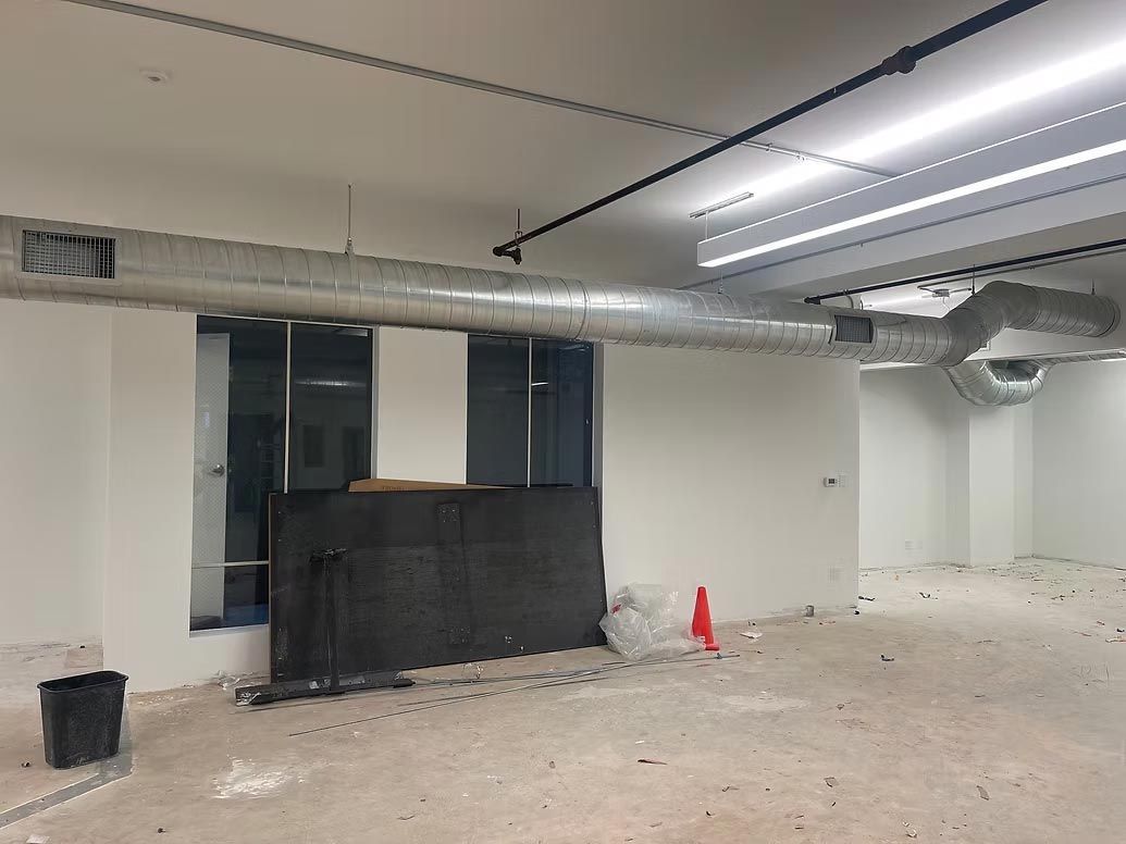 Empty unfinished room with exposed ductwork, windows, and debris on the floor