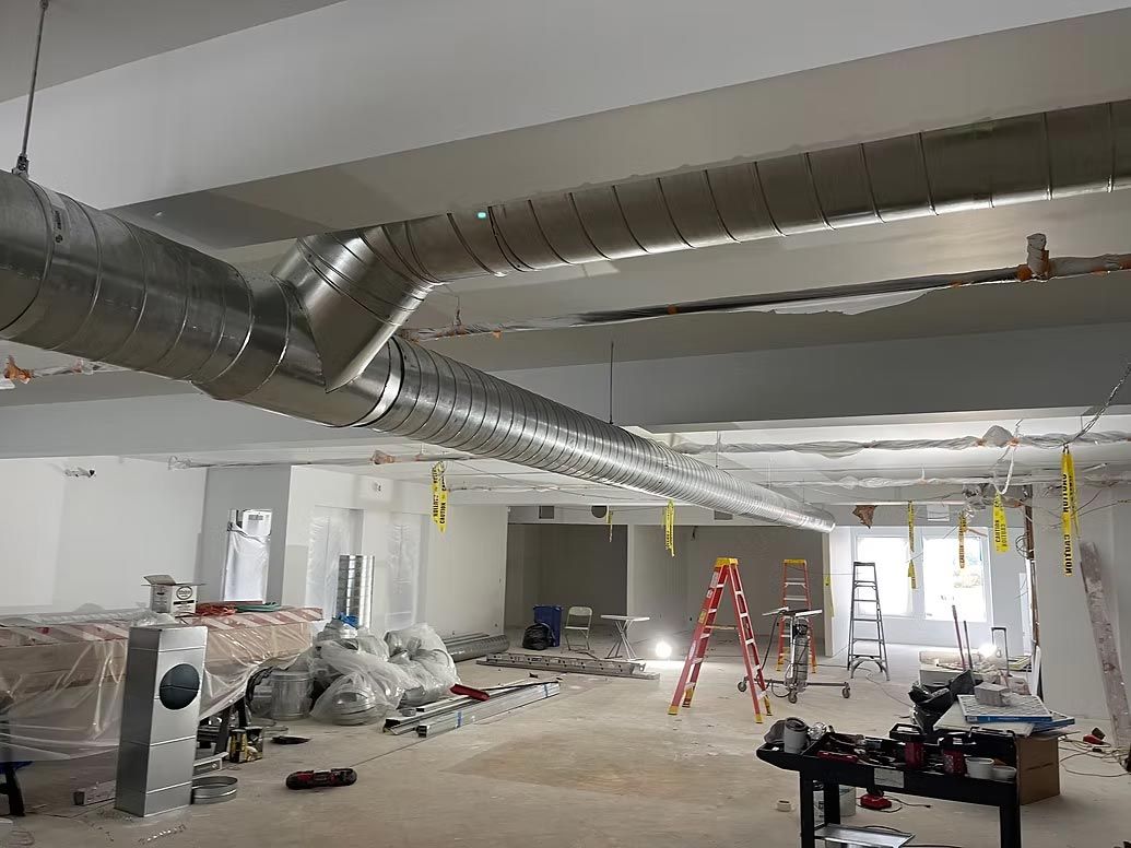 Interior of a construction site with exposed ductwork, ladders, and plastic-covered materials on the floor