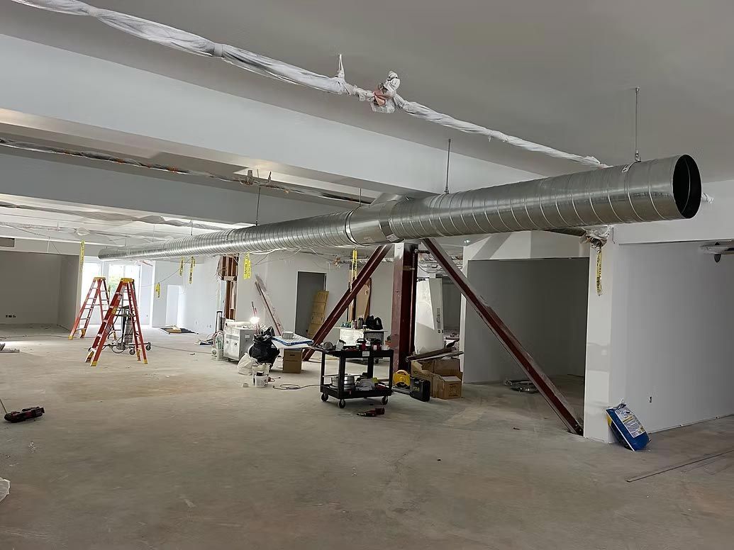 Construction site interior with exposed ductwork, ladders, and scattered equipment in a large unfinished room