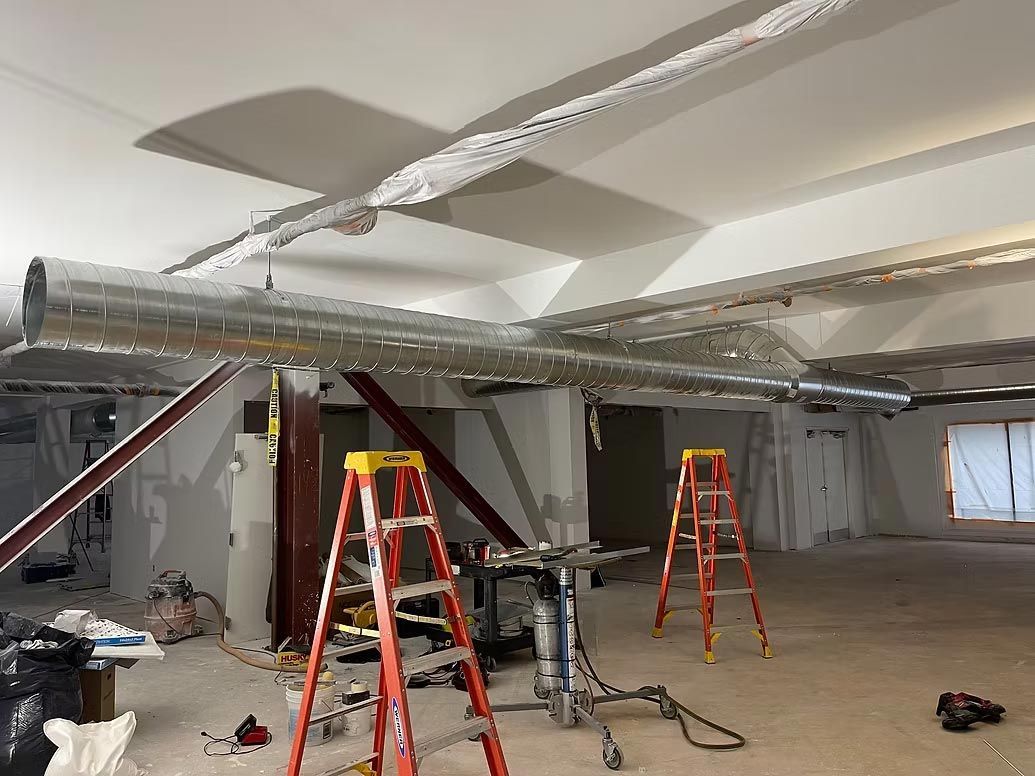 Indoor construction site with two red ladders, exposed ceiling beams, and scattered tools on the floor