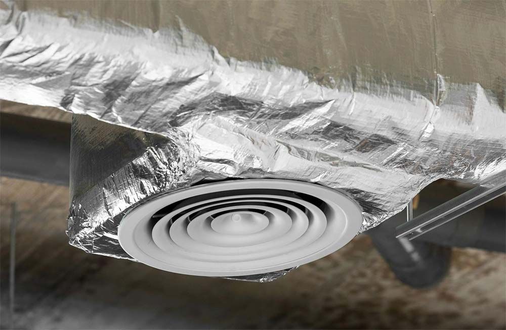 Circular air vent under a foil-wrapped surface, with silver duct insulation visible