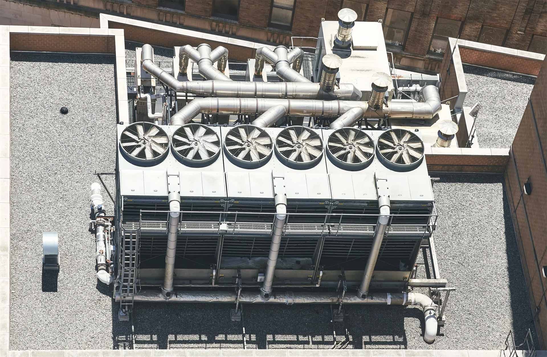 Rooftop industrial HVAC units and large fans on a gravel-covered roof