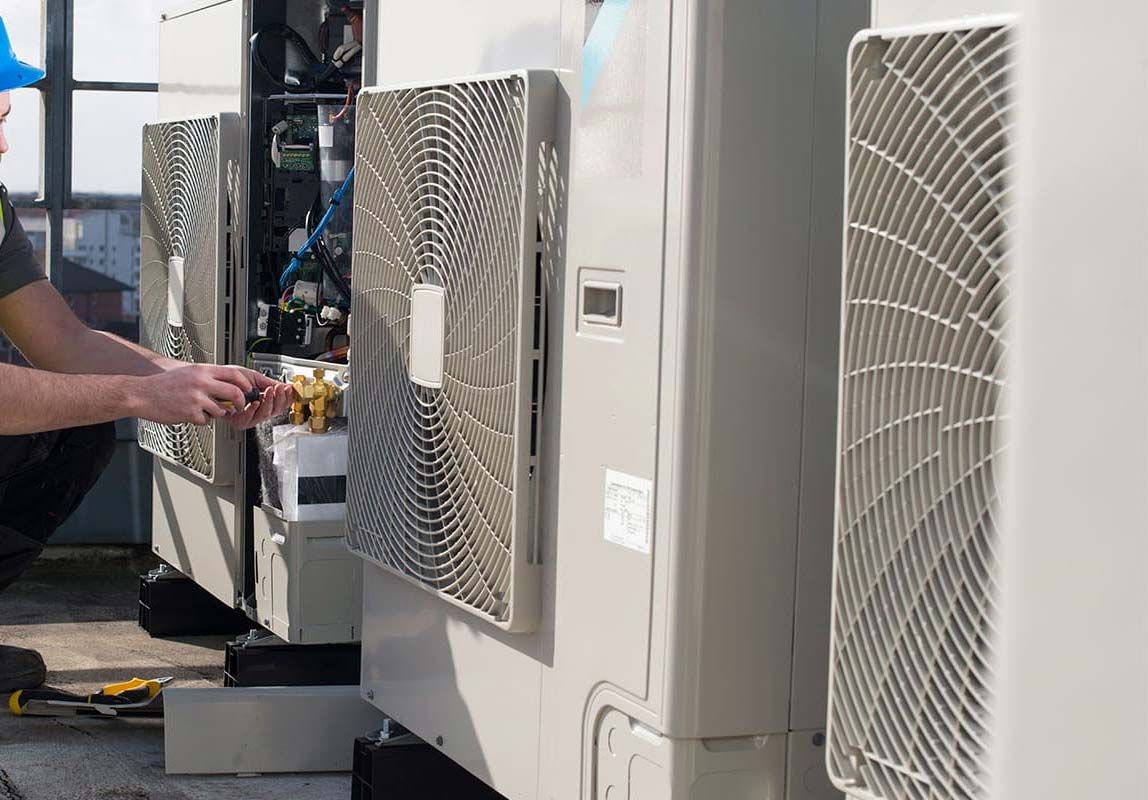 Person adjusting a cable near outdoor HVAC units in a utility area