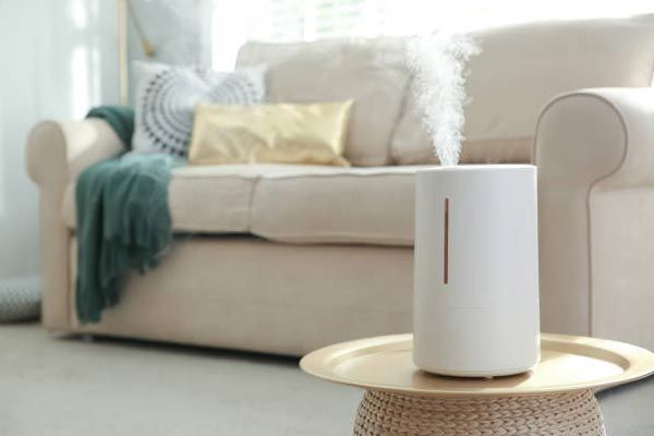 White humidifier steaming on a round table in a cozy living room with a beige sofa and teal throw blanket