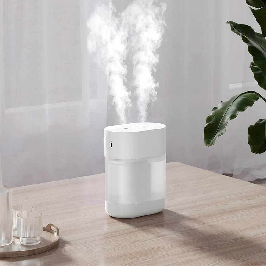 White tabletop humidifier releasing steam beside a plant and glass on a light wood table