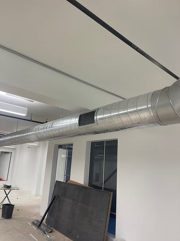 Office interior with exposed silver ductwork, white walls, and a window leaning against the wall.