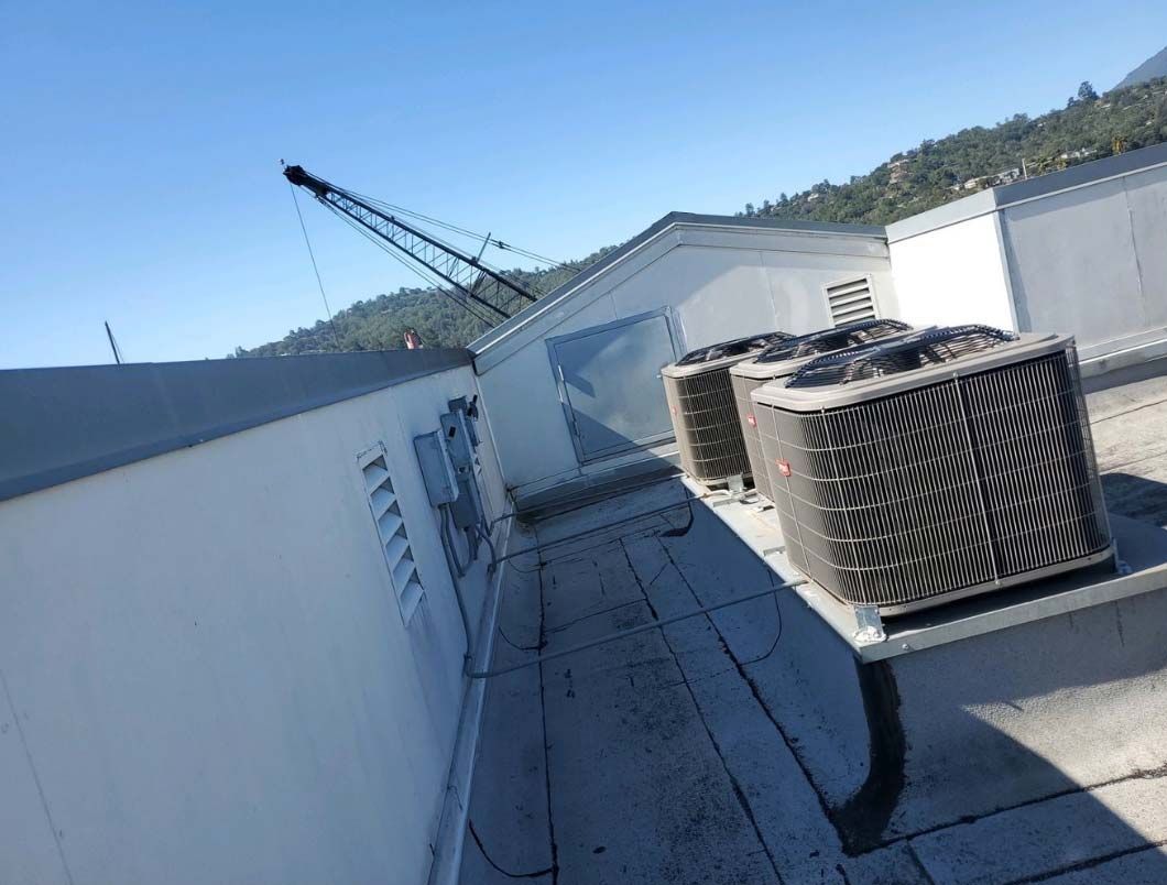Rooftop with HVAC units beside white walls, with a crane visible in the background.