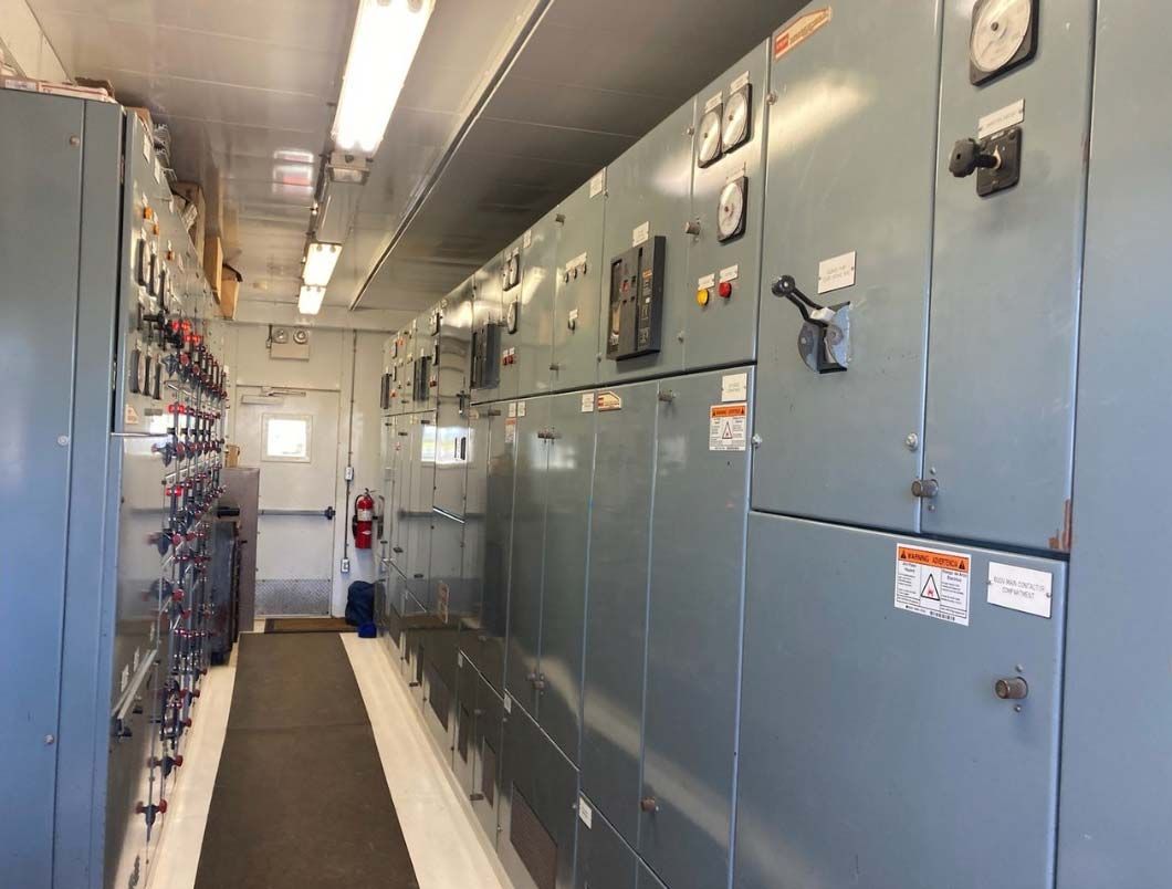 Narrow industrial corridor with blue electrical control panels along both sides and a red fire extinguisher at the end
