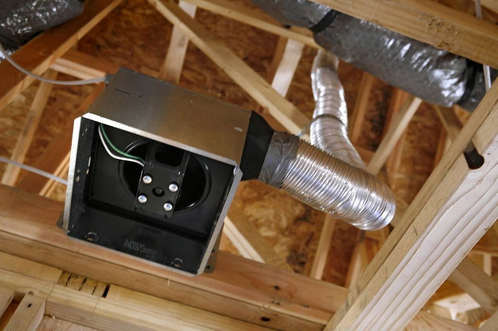 Open attic ceiling with a recessed light fixture and exposed ductwork among wooden rafters