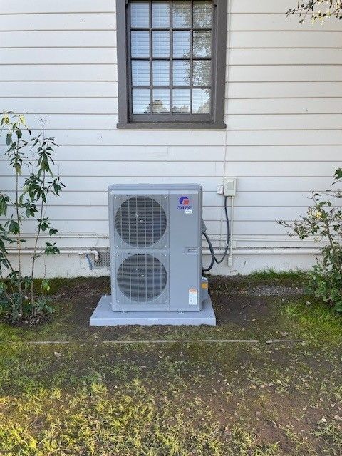 Outdoor heat pump unit beside a house window on a white siding wall