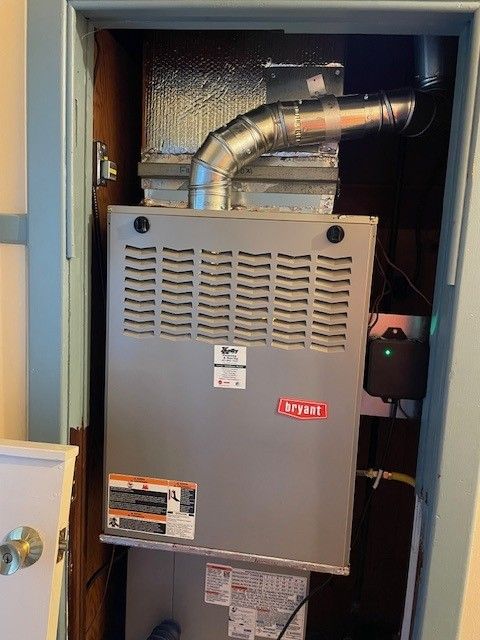 Open furnace in a closet, with metal venting and a gray Bryant unit inside.