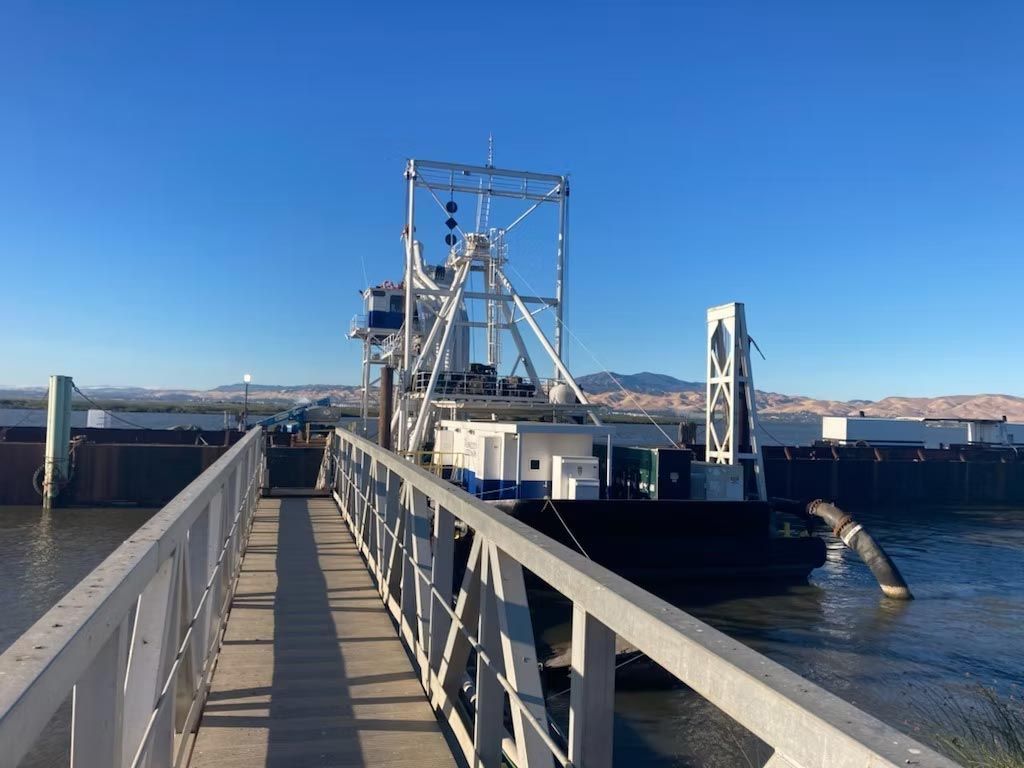 Gangway leading to a docked ferry or work boat on calm blue water under a clear sky