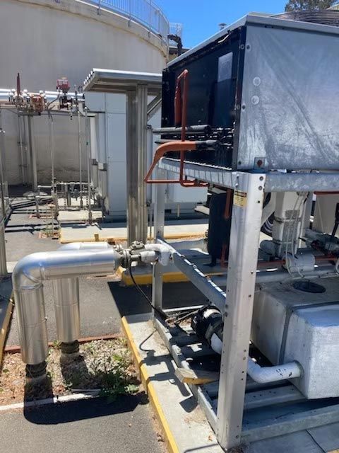Industrial rooftop HVAC unit with ducts, pipes, and metal equipment on a sunlit concrete platform