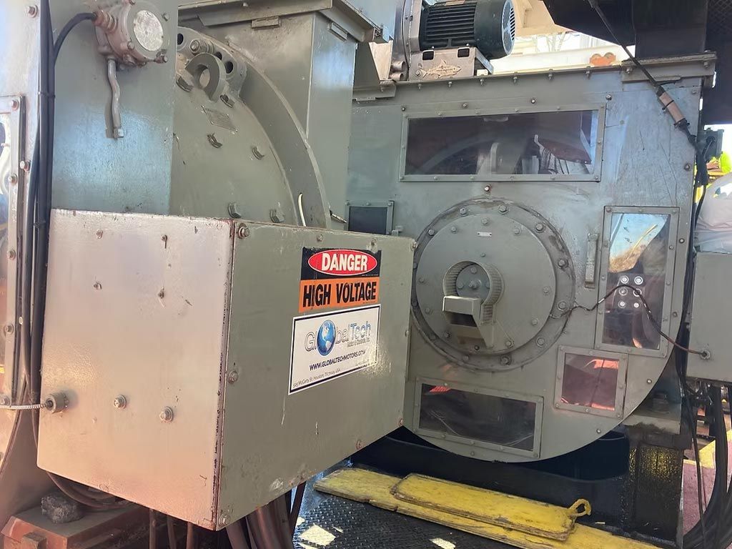 Industrial machinery with a gray metal housing and warning labels in a workshop setting