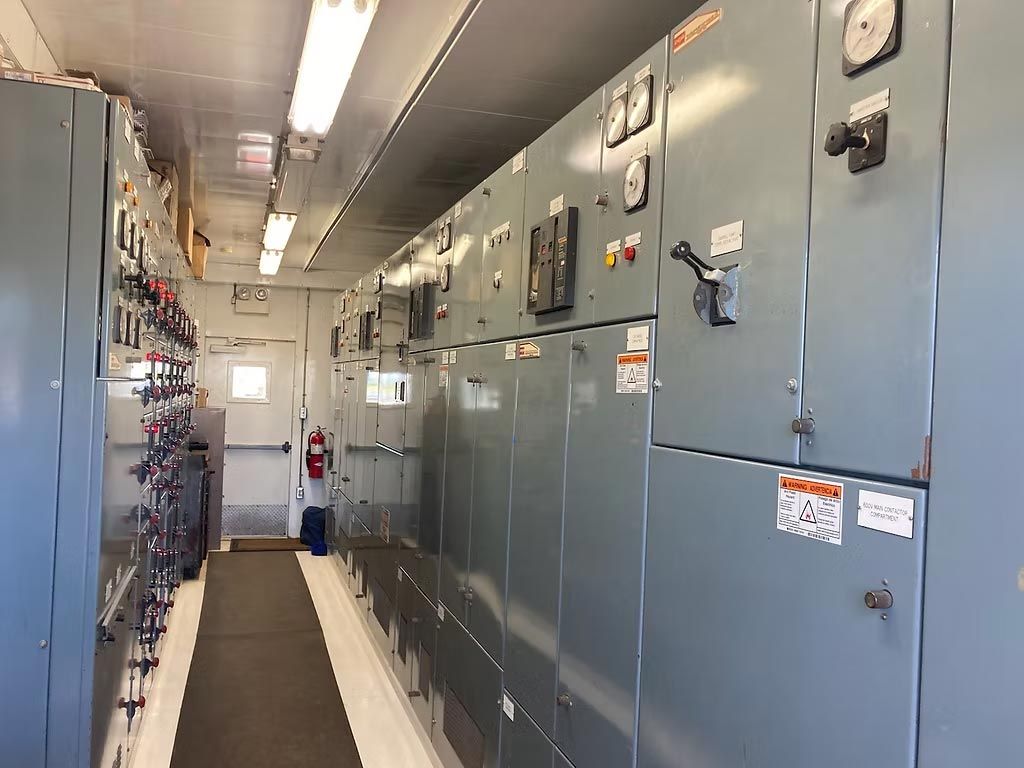 Narrow corridor lined with blue electrical control panels and gauges in an industrial facility