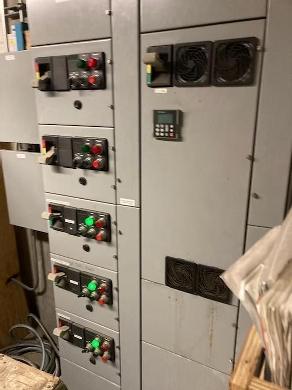 Electrical control panels with buttons, fans, and cables in a gray industrial room