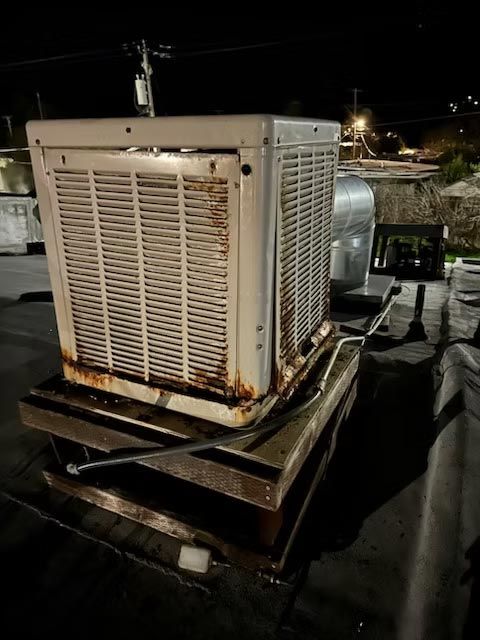 Rusty rooftop HVAC unit at night, with a white trailer in the background.