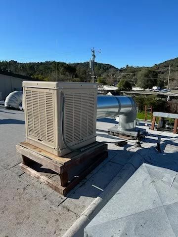 Beige rooftop HVAC unit on wooden pallets beside metal ducting under a clear blue sky.