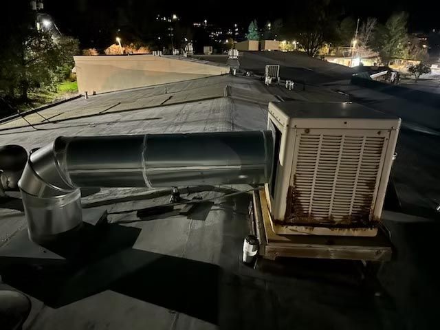 Night rooftop HVAC units and silver ductwork under dim city lights