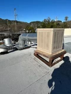 Rooftop HVAC unit on a wooden stand beside silver ductwork under a clear blue sky.