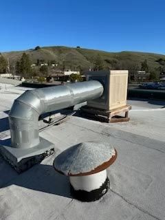 Silver rooftop HVAC duct beside a wooden crate, with hills in the background.