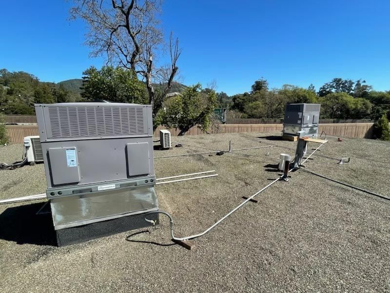 Two gray metal units on a dry field, connected by cables under a clear blue sky.