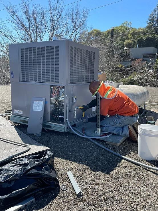 Worker in orange vest servicing a large rooftop HVAC unit on a sunny day.