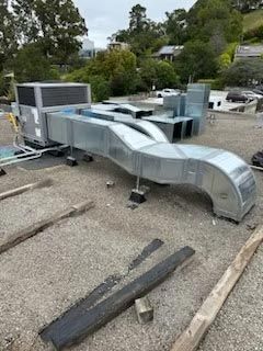 Silver rooftop HVAC ductwork on a gravel roof with trees and houses in the background