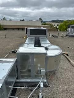Rooftop HVAC units and ductwork on a flat commercial roof under cloudy skies