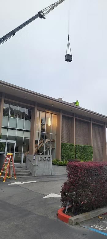 Crane hoisting a black load above a building entrance, with a ladder and workers below