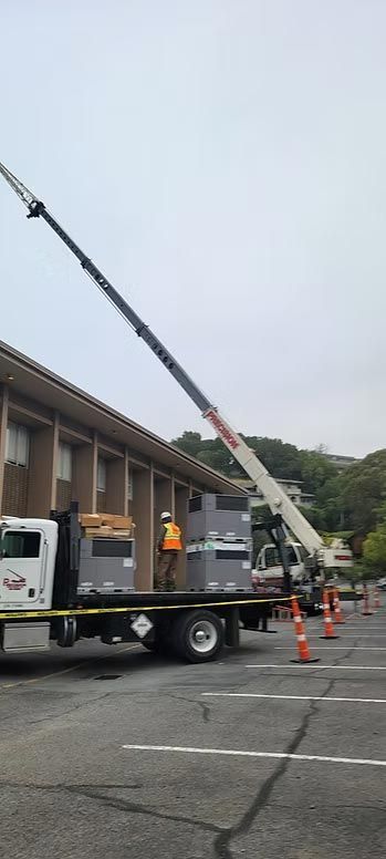 Utility truck with extended boom raised beside a building in a parking lot, with orange cones nearby