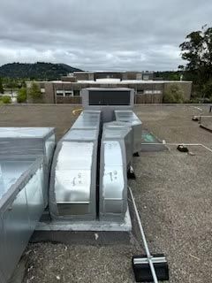 Rooftop HVAC ductwork and vents on a flat roof, with buildings and hills in the background
