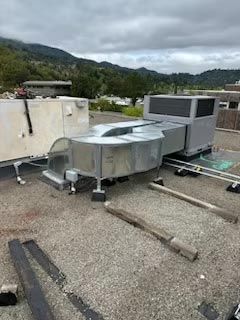 Rooftop HVAC unit and ductwork on a gravel roof with low walls and mountains in the background