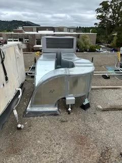 HVAC rooftop unit with silver ductwork on a gravel roof under cloudy sky