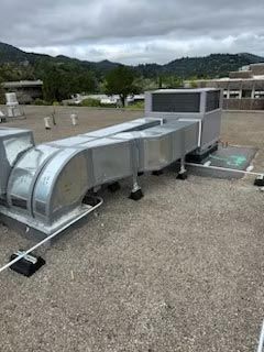Rooftop HVAC ductwork and metal unit on a gravel surface with mountains in the background