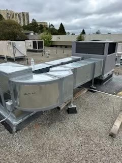 Rooftop HVAC units and ductwork on a gravel-covered commercial roof under cloudy skies