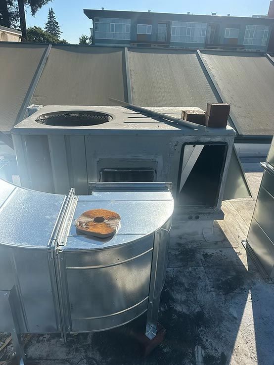 Rooftop HVAC units and ductwork on a flat industrial roof under bright sunlight.