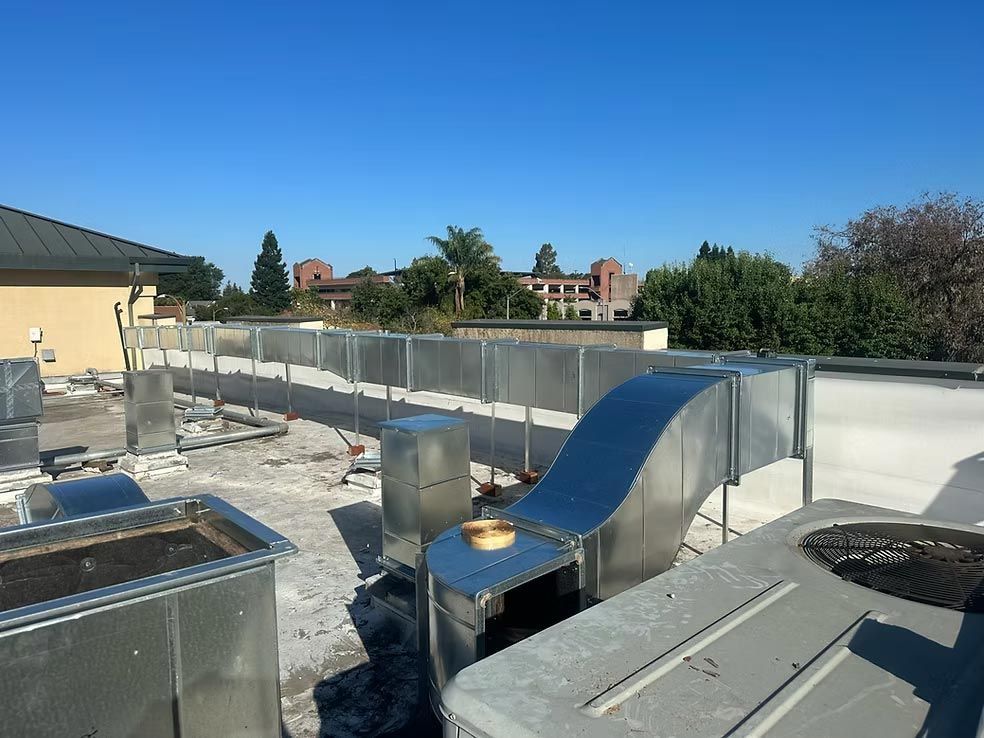 Rooftop with HVAC units, blue ducting, and a clear sky above a fenced mechanical area