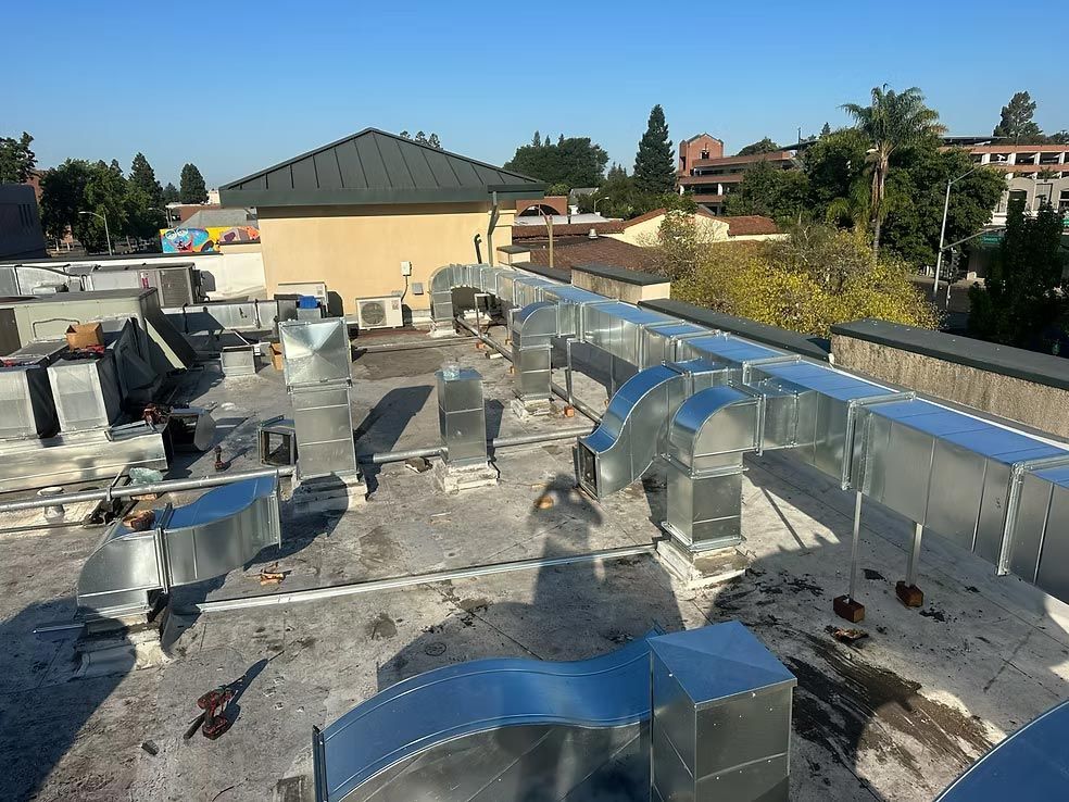 Rooftop with silver HVAC ducts and vents under a clear blue sky, surrounded by nearby buildings.