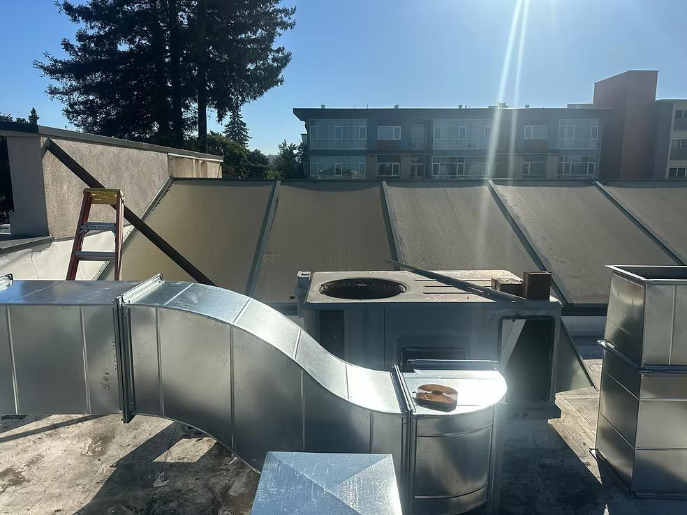 Rooftop HVAC ductwork and vents under bright sun, with apartment buildings in the background.